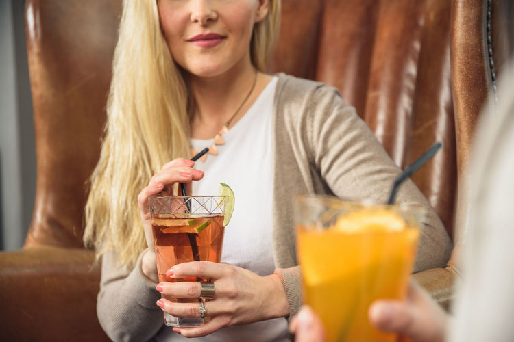 Crop woman drinking cocktail with friend