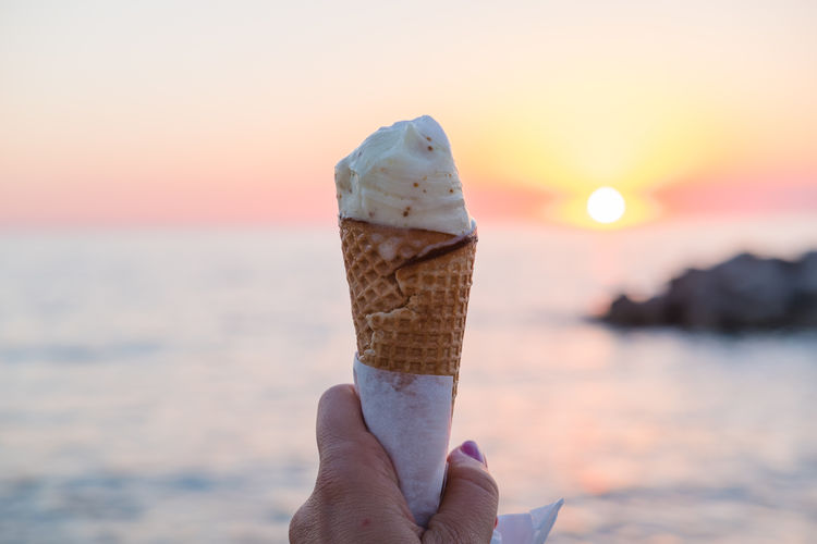 Close-up of hand holding ice cream at beach during sunset