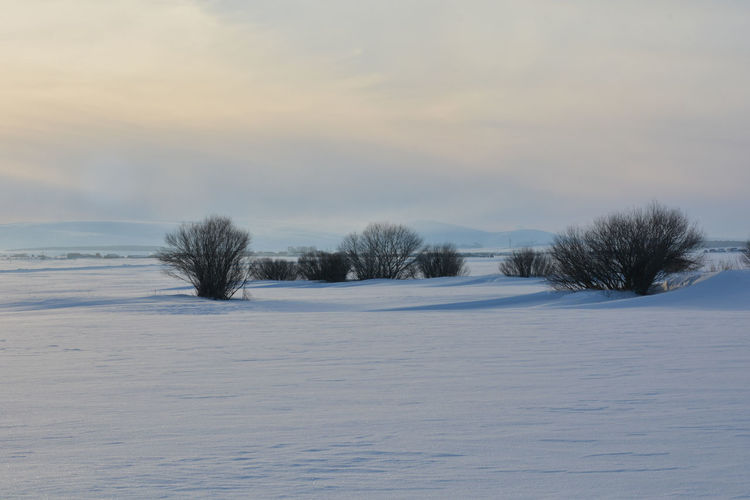 Snow covered field against sky at sunset