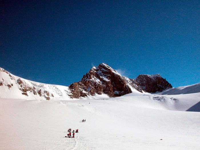 Group of people on snowcapped mountain against blue sky