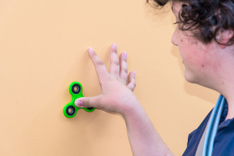 Close-up of boy holding fidget spinner against wall