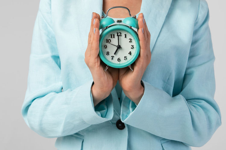 Close-up of woman holding clock over white background