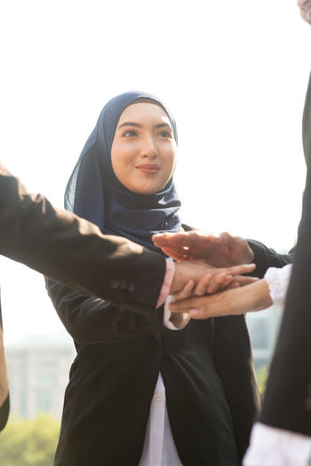 Smiling young businesswoman stacking hands with colleagues