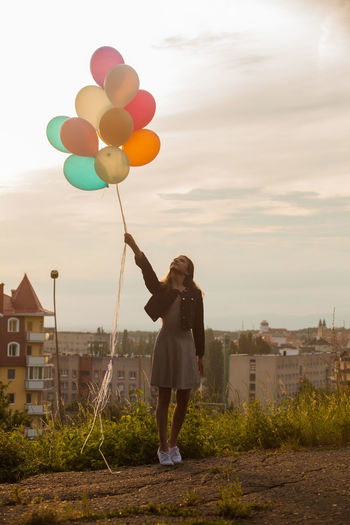 Teenager girl holding balloons standing against sky
