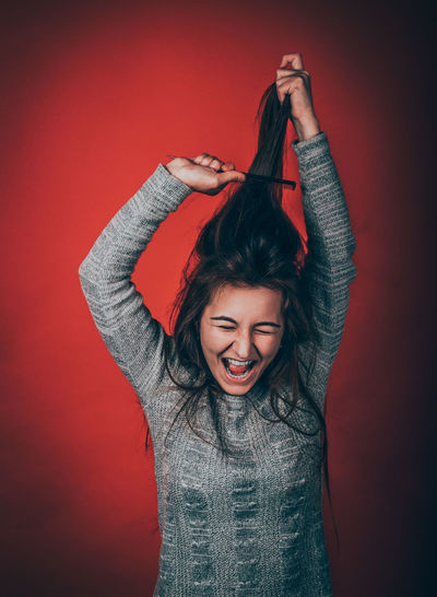 Cheerful young woman combing hair against red background
