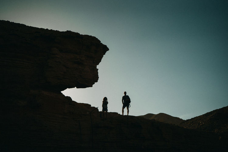 Low angle view of silhouette people on rock against sky