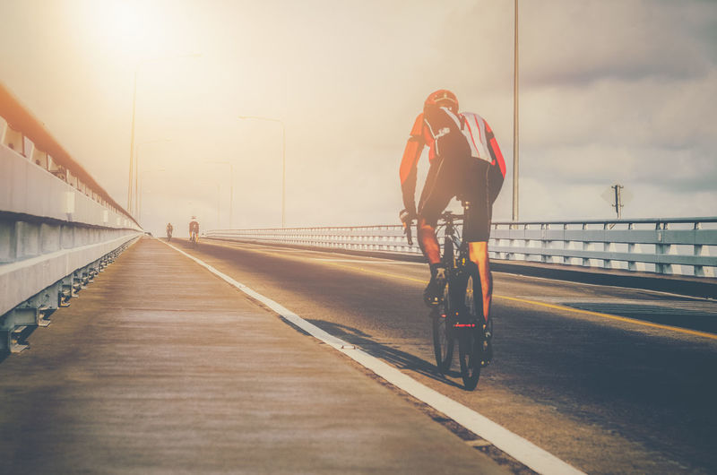 Rear view of sportsman riding bicycle on bridge against sky