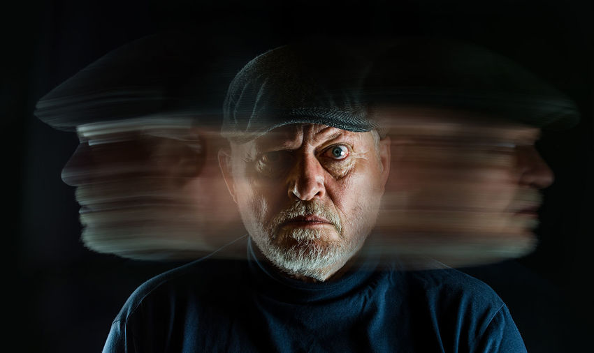 Blurred motion of angry senior man against black background