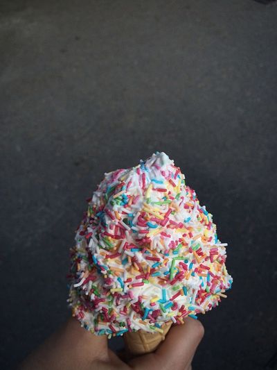 Close-up of hand holding ice cream cone against black background