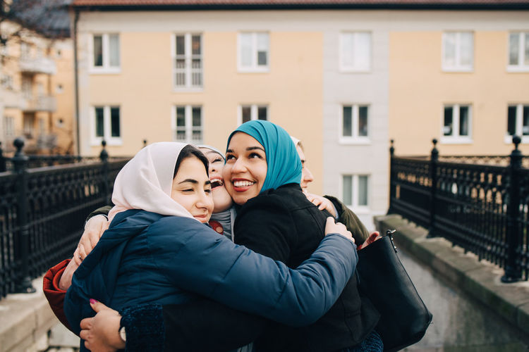 Cheerful multi-ethnic female muslim friends embracing in city