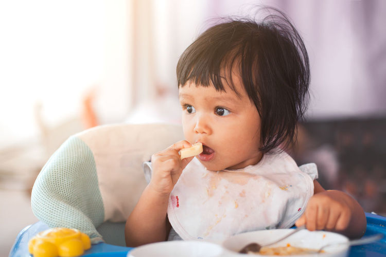 Close-up of baby girl eating food on high chair at home
