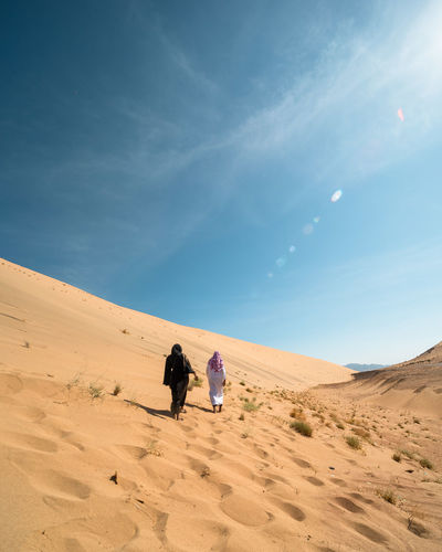 People on sand dune in desert against sky