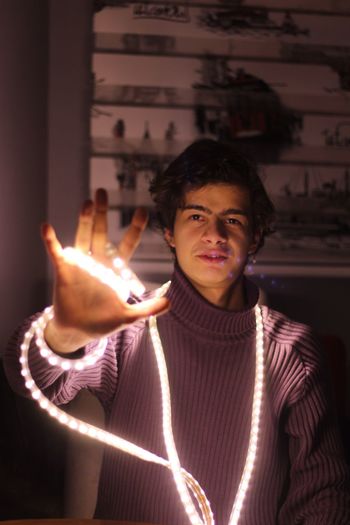 Portrait of man holding illuminated string light while standing at home