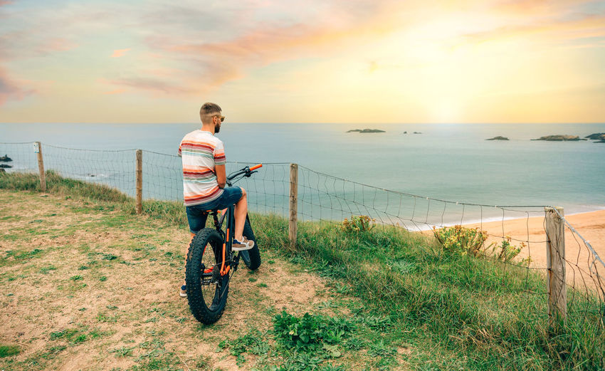 Young man riding a fat bike looking at the beach from the coast