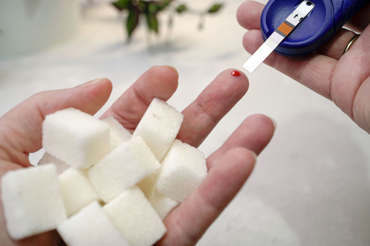 Cropped hands of person holding sugar cubes with glaucometer