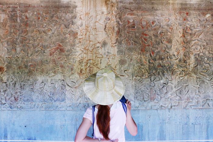 Rear view of woman looking at ancient text on angkor wat wall