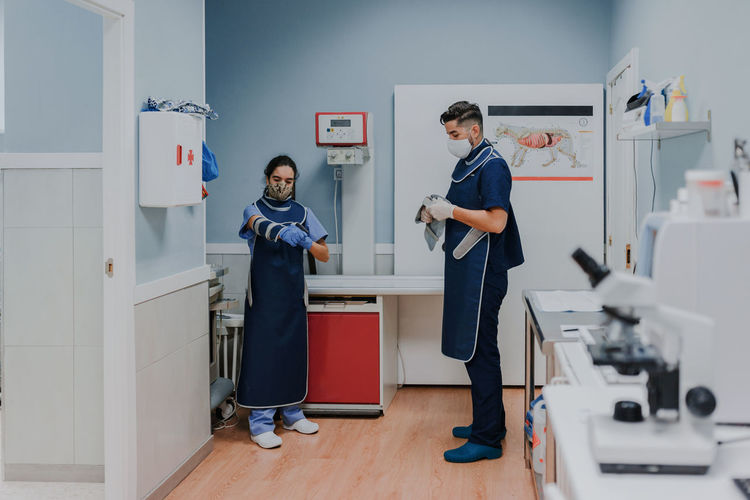 Unrecognizable young male vet in sterile mask and gloves standing near female colleague while preparing for work in lab