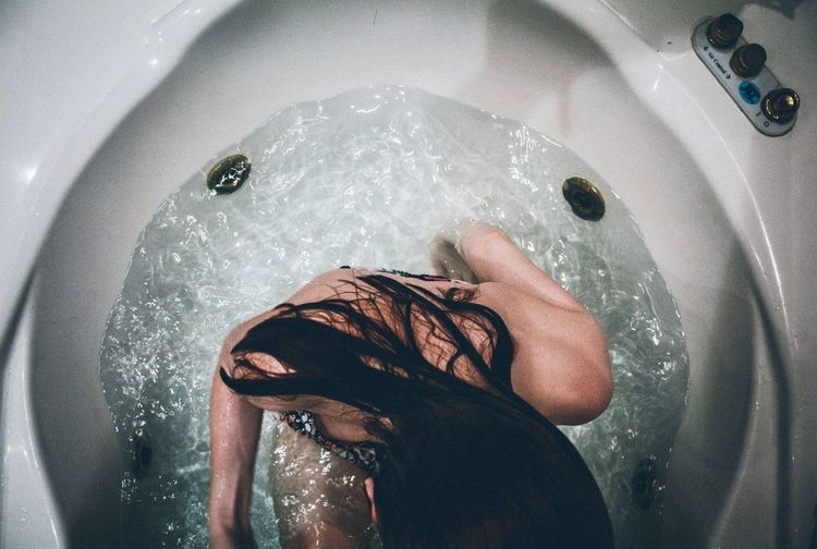 Overhead view of woman with long black hair sitting in bathtub