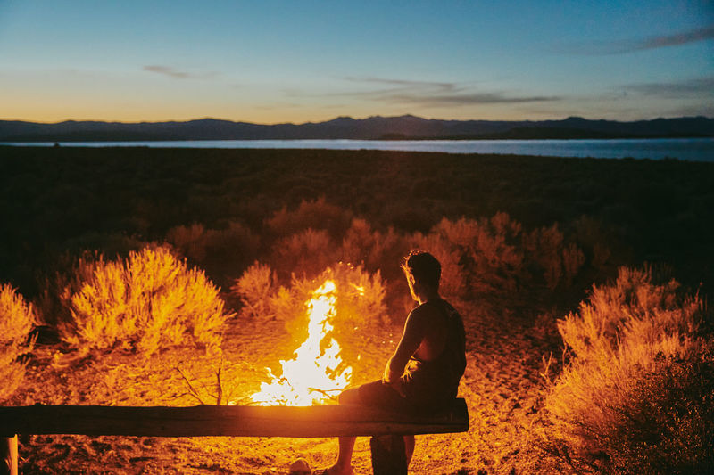 Young man sitting near campfire near mono lake at night in california.