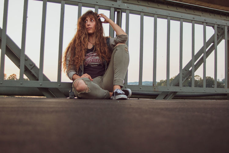 Portrait of young woman looking away while sitting on railing