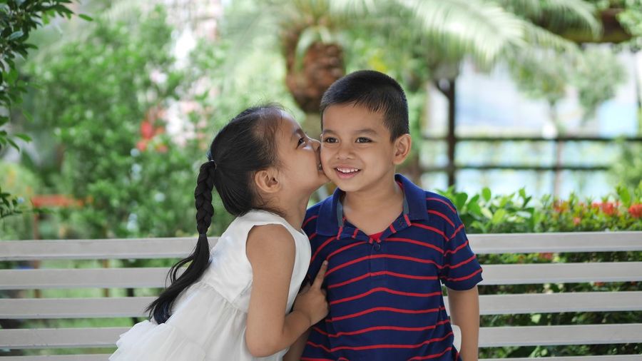 Smiling girl kissing brother on cheek while sitting on bench