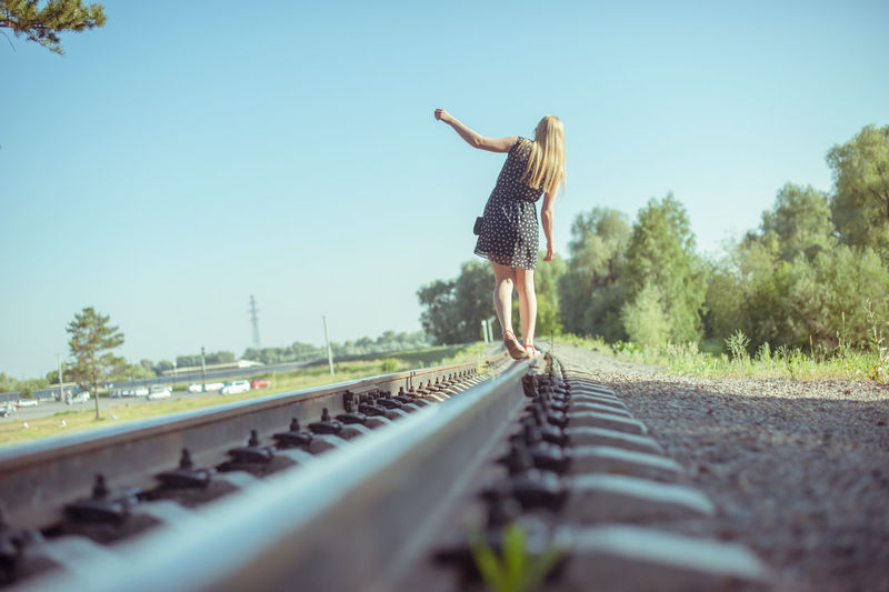 Rear view of woman on railroad tracks against clear sky
