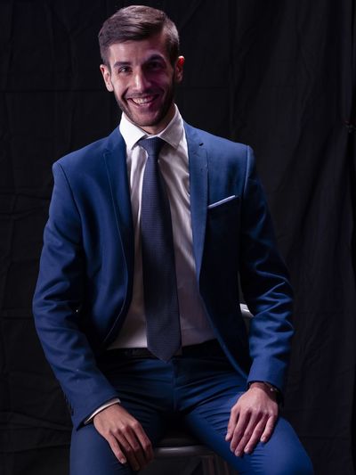 Portrait of smiling young man in suit sitting against black background