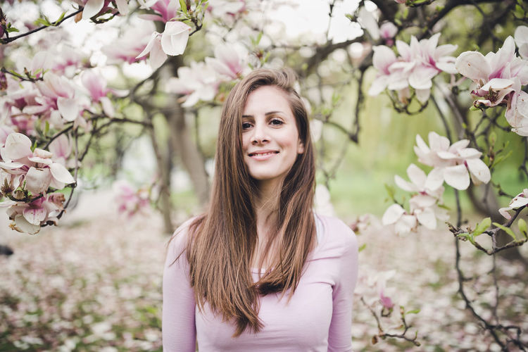 Cheerful long hair young ukrainian woman under the blooming magnolia in park. spring season 