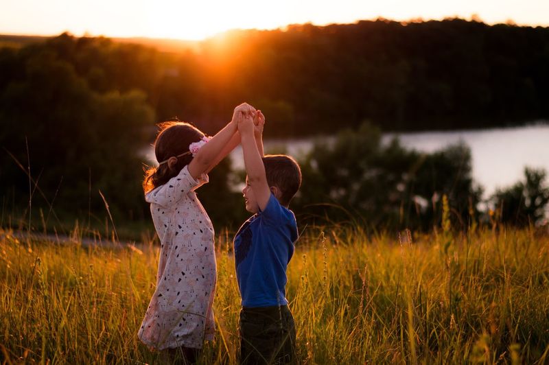 Children standing on field against sky during sunset