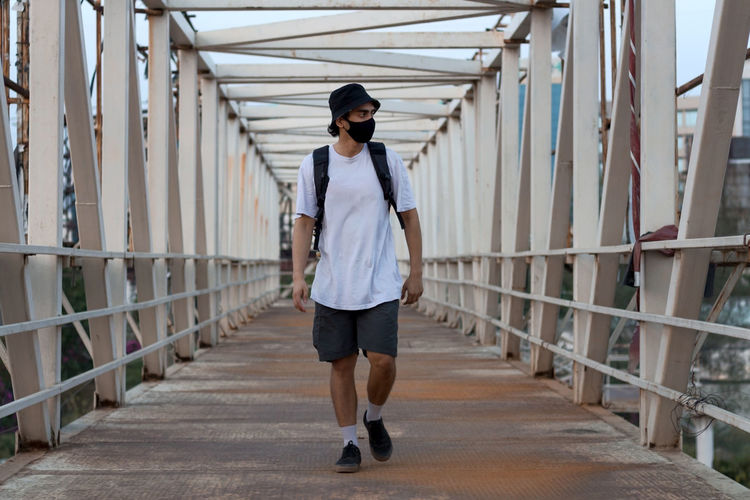 Young millennial walking on footbridge while wearing a protective mask to prevent covid-19 infection