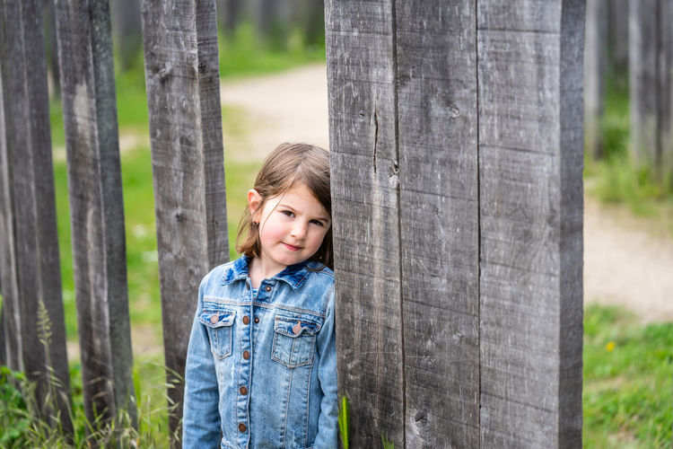 Portrait of smiling girl standing by plank outdoors