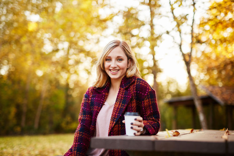Young woman sitting on picnic table in park during autumn