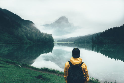 Rear view of man looking at obersee lake by mountains in foggy weather