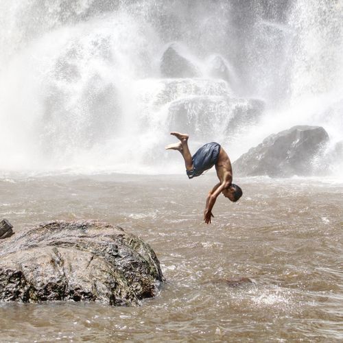 Side view of man jumping in waterfall