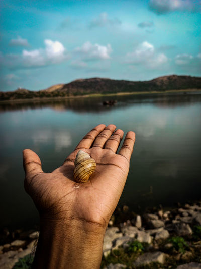 Close-up of human hand against lake