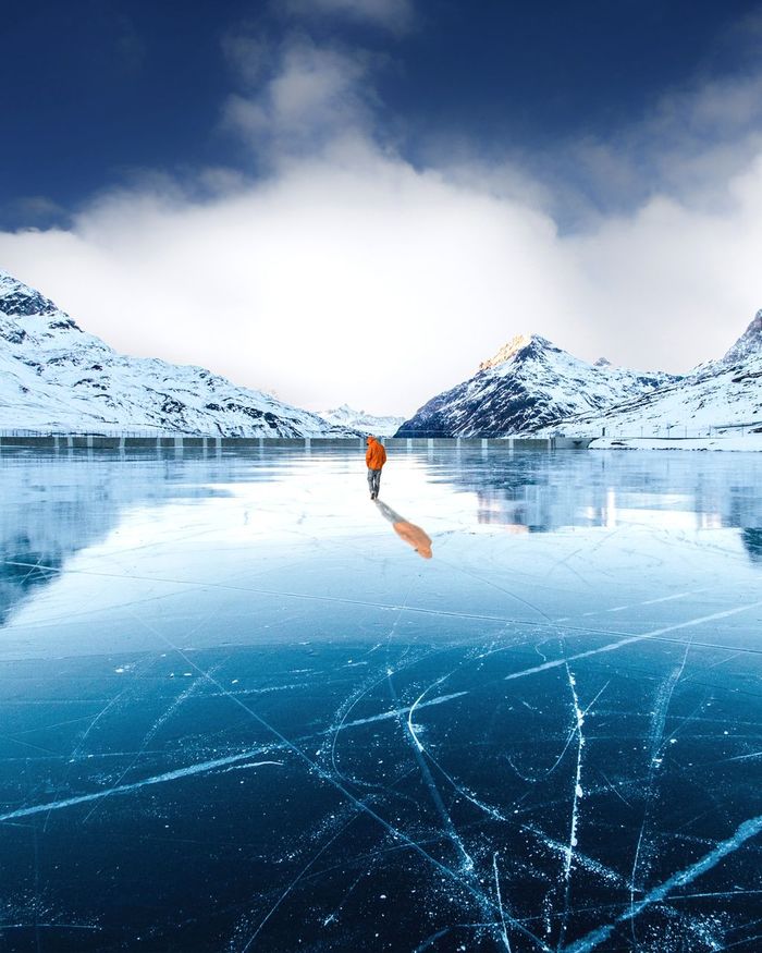 Man standing by frozen lake against mountain during winter
