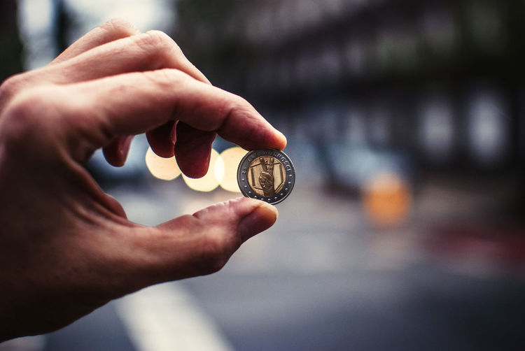 Cropped image of person holding coin between thumb and finger