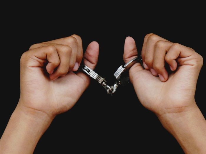 Close-up of man with small hand cuffs over black background