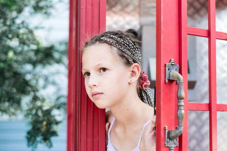 A sad little girl with afro-braids looks out from an old english telephone booth