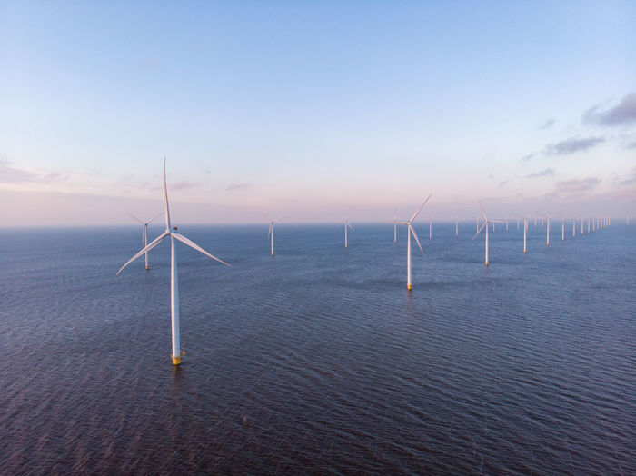 Wind turbines in sea against sky during sunset, windmill turbines in the netherlands 