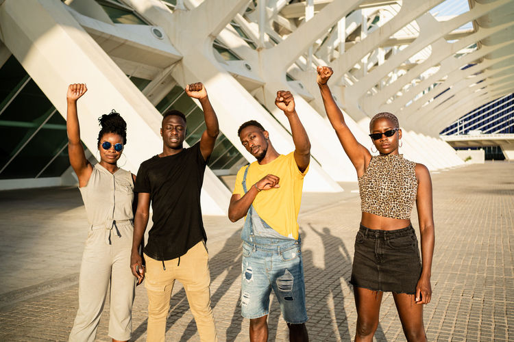 Company of african american friends standing in city with fists up and confidently looking at camera while showing power and expressing solidarity