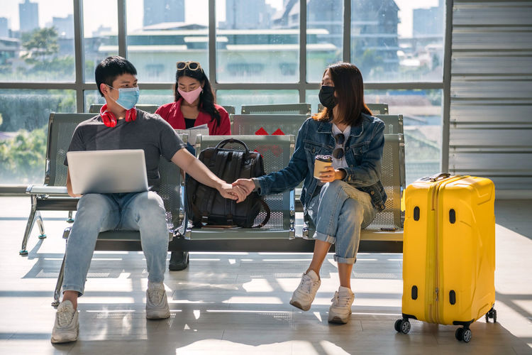 Man and woman wearing mask holding hands sitting at airport