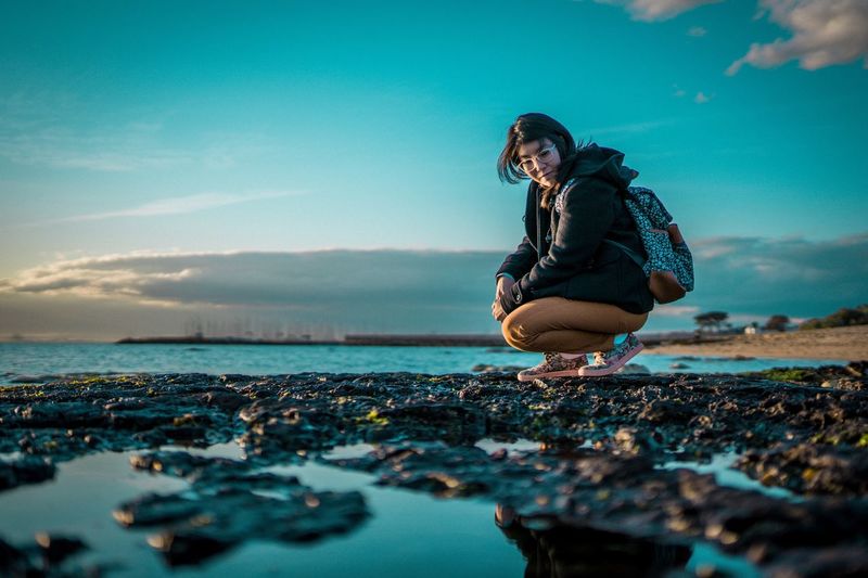 Woman crouching at beach against sky