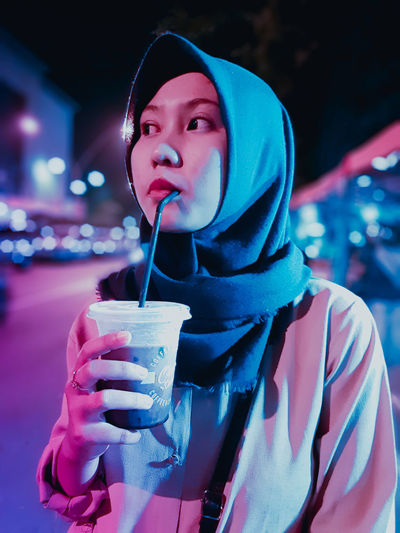 Young woman looking away while drinking coffee outdoors