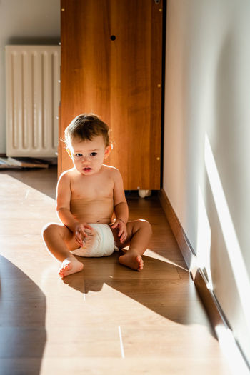 Cute baby girl sitting on wooden floor at home