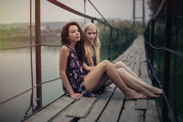 Lesbian couple sitting on footbridge against sky
