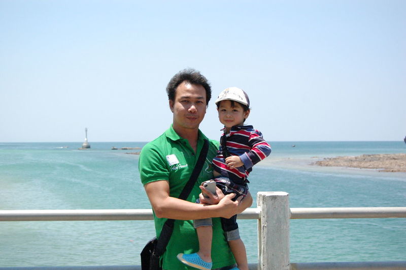 Portrait of father carrying son while standing against sea