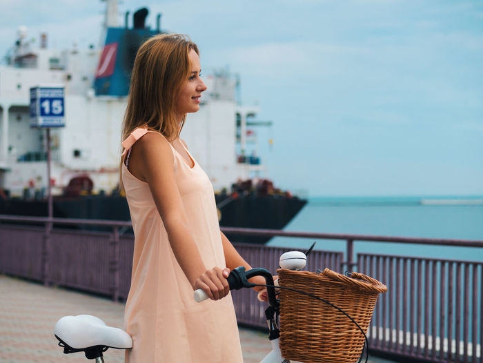 Side view of beautiful woman with bicycle looking away while standing at promenade