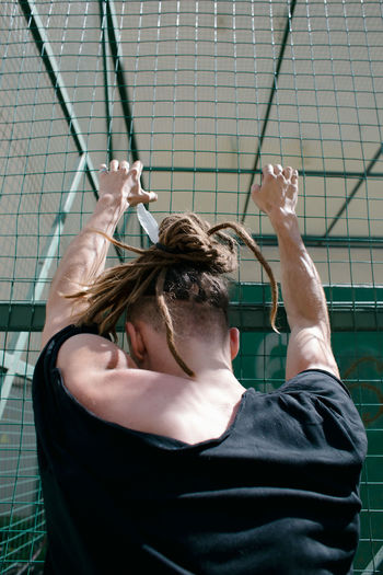 Rear view of muscular man climbing on fence