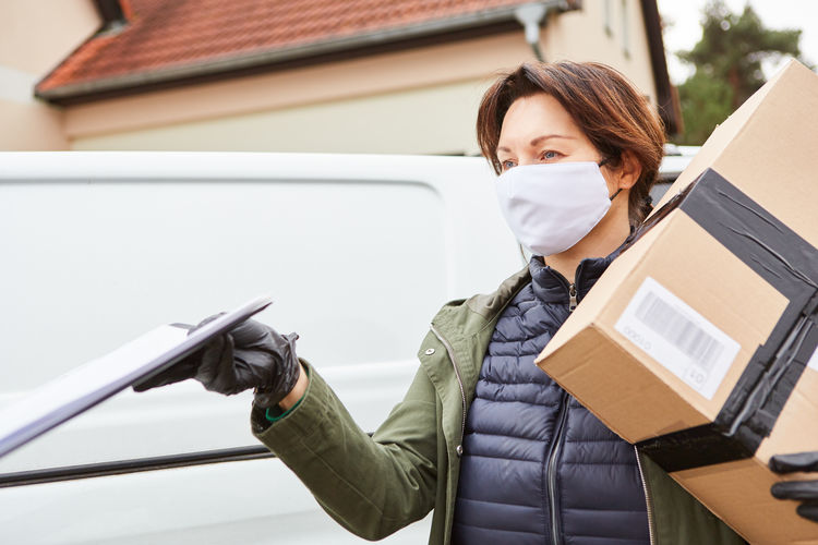 Close-up of delivery person wearing mask carrying parcel
